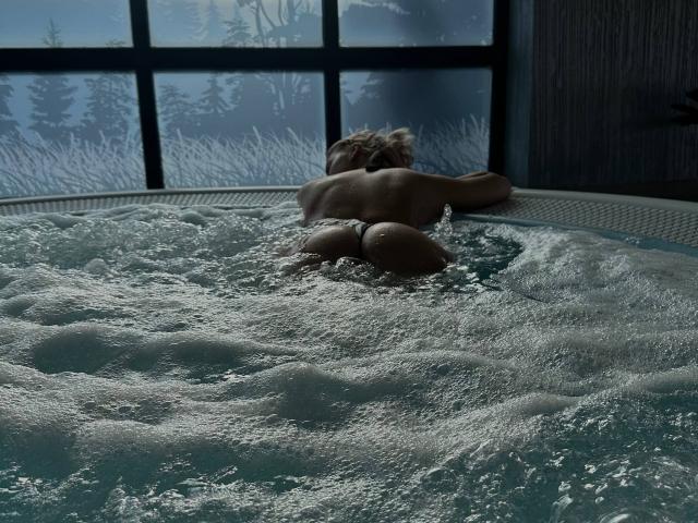 LeylaBunny, naked, with her back to the camera, lies in a bubbling hot tub, her wet ass and butt cheeks visible, arms resting on the edge.