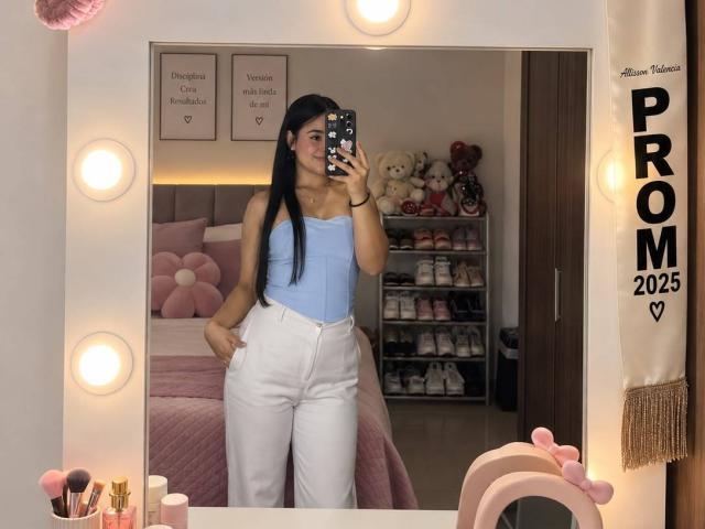 MalloryRamos with long black hair, wearing a light blue strapless top and white high-waisted pants, standing in front of a mirror, showing her ass and small tits.