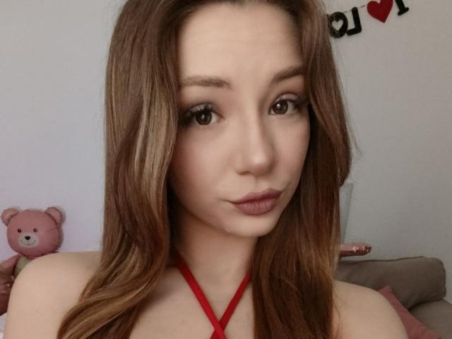 AmandaGrasy ha la pelle chiara, gli occhi marroni e i capelli lunghi castani, indossa un top rosso con spalline, ha le labbra rosa ben disegnate e sullo sfondo c'è un simpatico orsetto rosa..