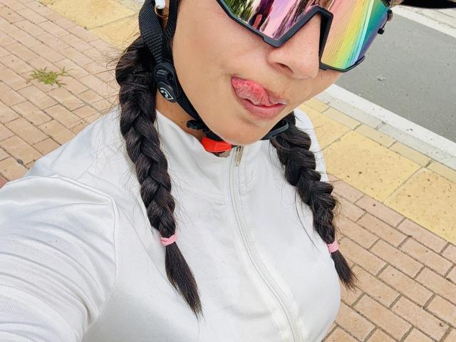 KimmyK with braided black hair, white zip-up, rainbow reflective sunglasses, and tongue out, wearing a black helmet with white ear pads, showing her tits slightly.