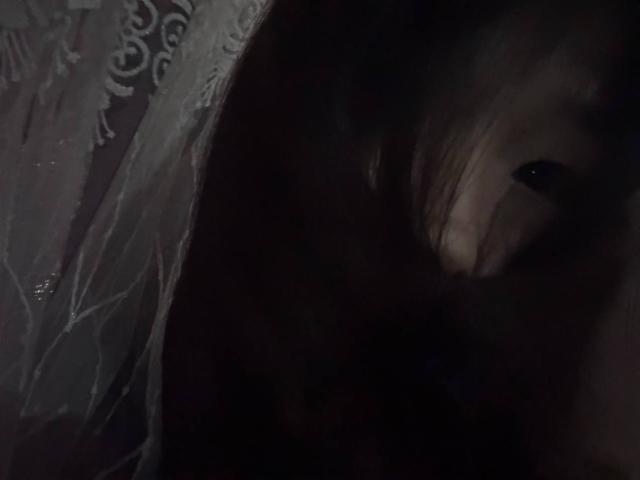 El rostro de JungMcgranor, de cabello oscuro, se vislumbra parcialmente en la penumbra, con sus ojos mirando de lado, transmitiendo una vibra misteriosa y sombría. El tejido transparente y los tonos oscuros realzan la apariencia inquietante y oculta..