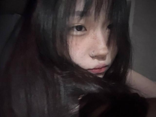 JungMcgranor hat dunkles, zerzaustes Haar, eine Nasenpiercing und ein leicht schmollendes Gesicht, mit dunklen Augen, die nach unten schauen. Ihre helle Haut und rote Lippen sind sichtbar..