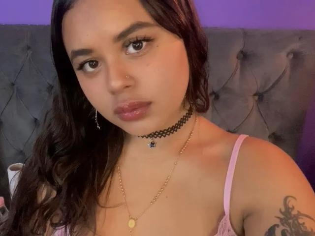 ChiaraBella hat dunkles Haar, braune Augen und rosafarbene Lippen. Sie trägt einen schwarzen Choker, eine goldene Halskette und einen pinken BH. Sie hat ein Tattoo an ihrem rechten Arm..