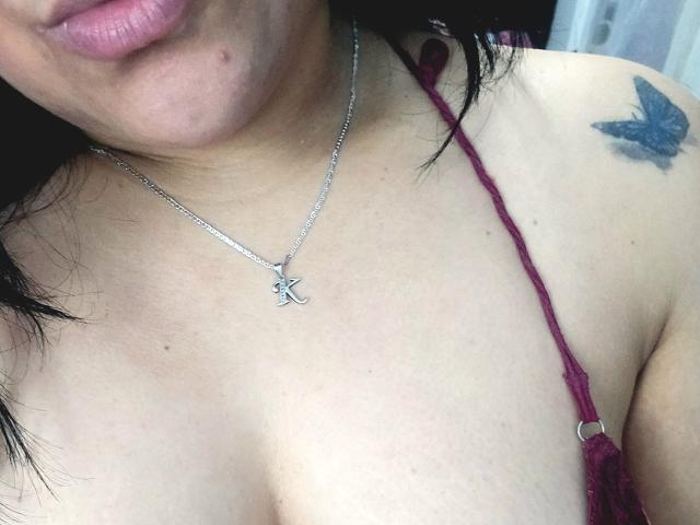 VivianaThomson's upper chest with a silver necklace, a small tattoo of a blue butterfly on her right shoulder, and her pink lips, showing her cleavage in a red strap.