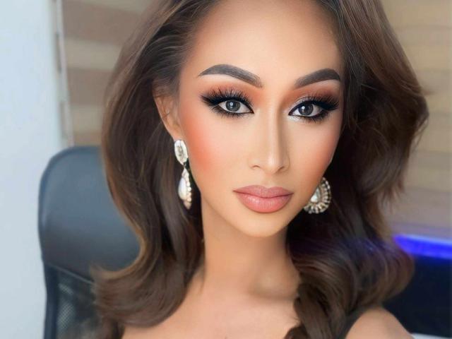 TsLavander has dark brown wavy hair, full eyebrows, smokey eye makeup, long lashes, pinkish nude lipstick, and is wearing large, shiny, teardrop earrings with a serious expression.