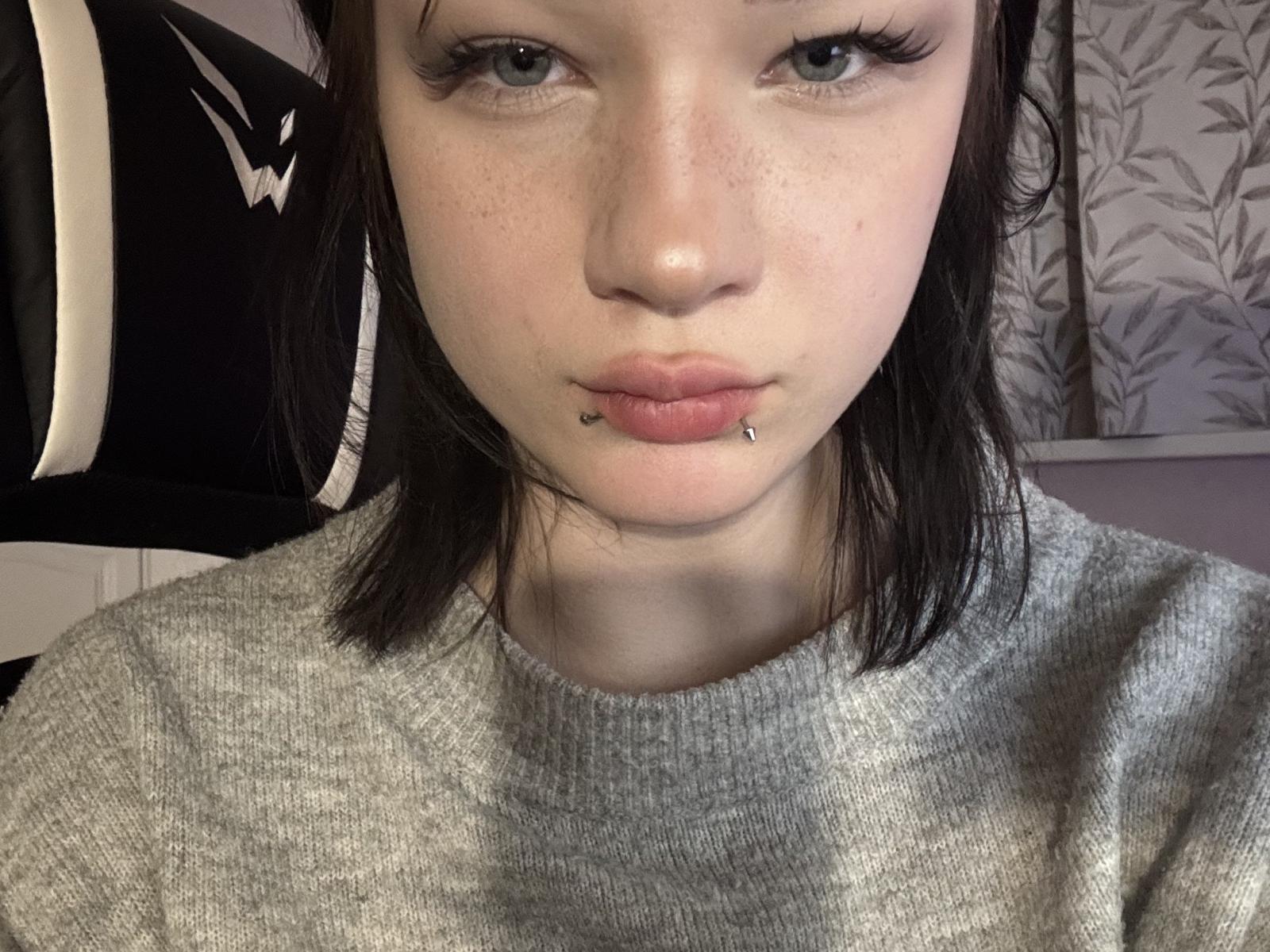 IvanaHahne heeft een lichte huid, sproeten, zwart haar, blauwe ogen en ze frumelt, met een lip piercing en een andere piercing onder haar onderlip. Ze draagt een grijze trui..