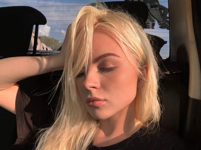 JerleneLeoni has blonde hair, fair skin, and closed eyes, with her hand in her hair, showing off her pouty lips and subtle makeup. She's sitting in a car.