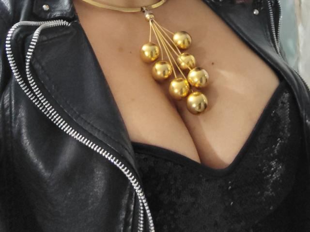 VioletaSwitch's big tits in a black lace top, covered by a black leather jacket, with a gold necklace of dangling bells.