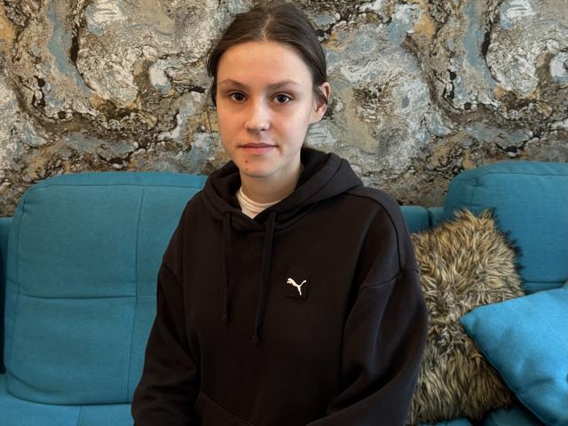 GracyMurre mit braunen Haaren, einem schwarzen Puma-Hoodie und einem ernsten Gesicht, sitzt auf einem blauen Sofa mit einem flauschigen Kissen. Ihre Brüste sind klein, und sie sieht süß aus..