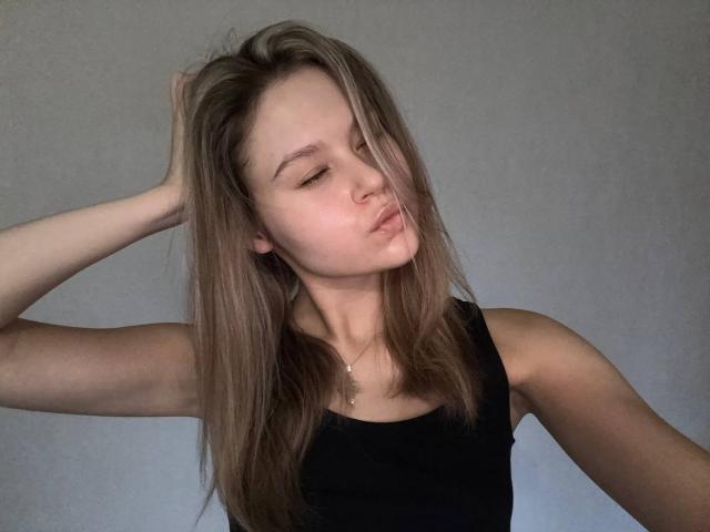 YungQuiller has light brown hair, a black sleeveless top, and is pouting with eyes closed, touching her hair with one hand. She's wearing a thin necklace.