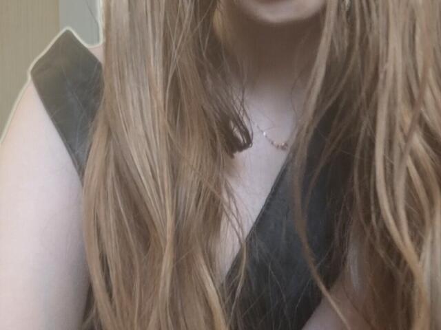 ElzaKomx's upper body, showing long, wavy brown hair, black sleeveless top, and a delicate necklace, with a slight focus on her tits and chest.