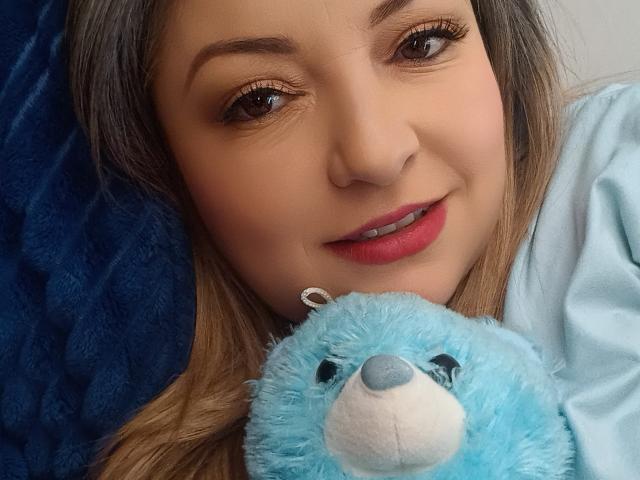 Il viso di NatalyHami, con la sua pelle marrone chiaro, il rossetto rosso e gli occhi marroni, mentre tiene un orsacchiotto blu soffice con il naso bianco. Ha i capelli lunghi e marroni e un orecchino d'argento..