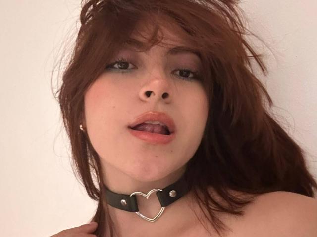 SpencerLe a les cheveux bruns et indisciplinés, un piercing au nez et un collier en cuir noir avec une boucle métallique en forme de cœur. Elle tire la langue. Ses seins ne sont pas visibles..