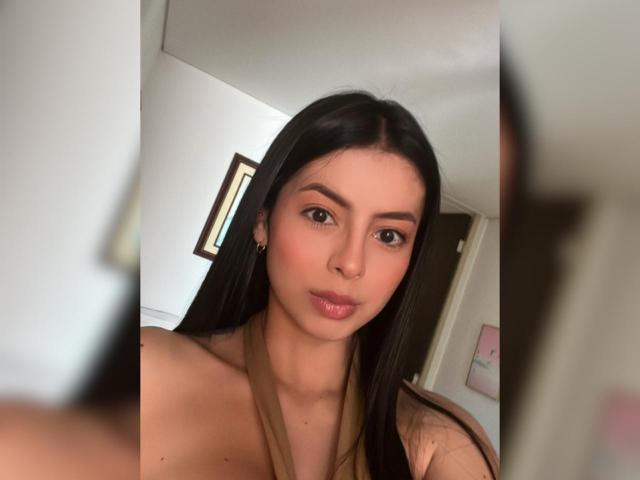 IsabellaJames with long black hair, brown eyes, and light skin, wearing a tan halter top, showing her small tits, and pouty lips in a selfie.
