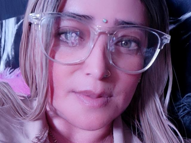 Alessadra Joness, mit Brille, Nasenring und einem kleinen Punkt auf der Stirn, der an einem dritten Auge erinnert, hat einen leicht rosafarbenen Hautton und blondes Haar, und wirkt etwas traurig, mit kleinen Brüsten..