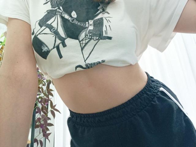 WollyMolly's midriff with a white crop top showing black print, black sports shorts with white stripes, and a small red mark on their pale skin.