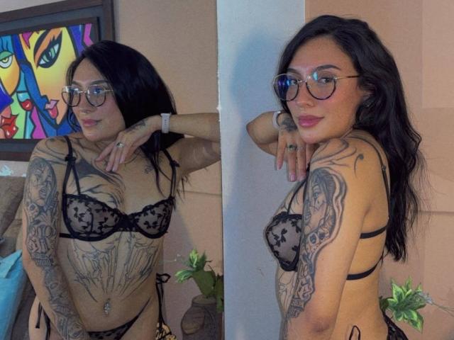 SophiieBlair with tattoos, black lace bra, and panties, glasses, long black hair, side and front poses, showing tits and tattoos, pouty lips, and a confident look.