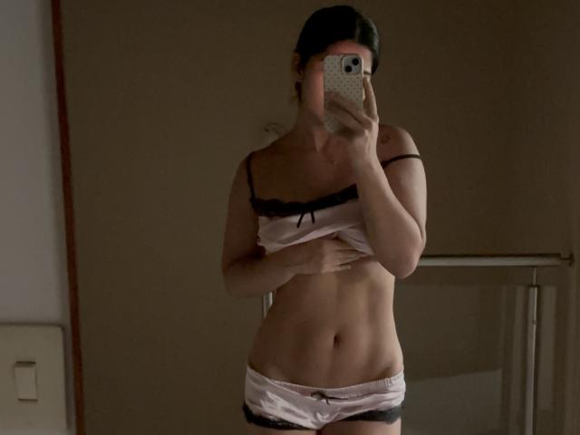 ScarlletZhen, con piccoli seni, indossa biancheria intima in seta rosa con pizzo nero, e si scatta un selfie allo specchio, coprendo il seno destro con la mano e tenendo il telefono nella mano sinistra..