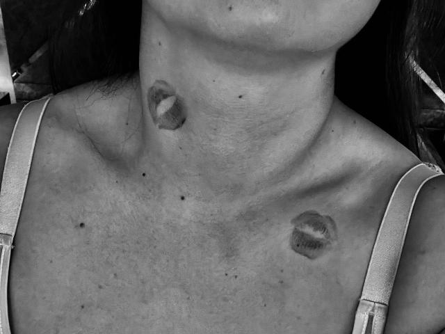Fotografia in bianco e nero del collo e del petto di DariaCalm, che mostra due tatuaggi labiali: uno sul collo e uno sul petto, e indossa una maglietta a spalline. Seno, collo, petto..