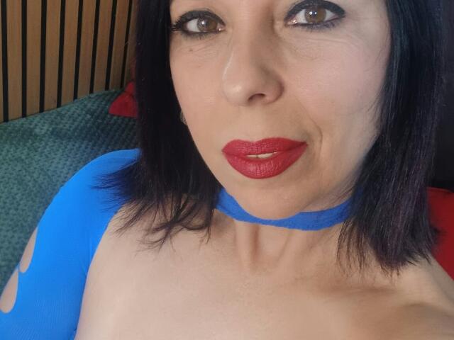 LauraSin, avec du rouge à lèvres, des cheveux noirs mi-longs et un haut bleu, regardant la caméra avec les lèvres légèrement entrouvertes, montrant sa poitrine nue et sa clavicule..