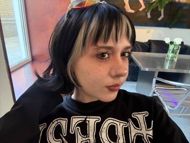 KrystalBerkovitch has black and blonde hair, a nose ring, facial piercings, and a black "Victory" shirt, sitting indoors with sunglasses on her head.