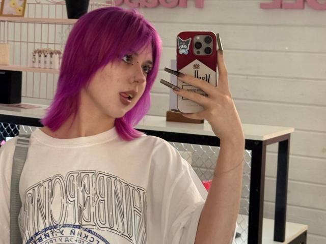 KrystalBerkovitch with bright purple hair, white tee, and long black nails, taking a mirror selfie with a red phone, showing off her ass.
