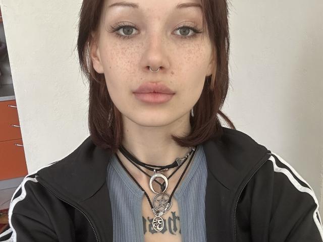 AlineGossom heeft een huid met sproeten, bruine ogen en een neusring. Ze draagt een zwarte jas met witte strepen, een blauw shirt en meerdere kettingen met een ring en een hanger..
