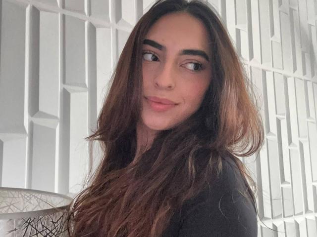 CelesteLarson a de longs cheveux bruns, des sourcils épais et un léger sourire. Elle porte un haut noir et regarde sur le côté, les yeux à moitié fermés. Ses lèvres sont d'un rose tendre..