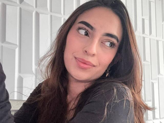 CelesteLarson has long brown hair, full eyebrows, and a slight smile. She's wearing a black shirt, looking to the side with pink lipstick and small hoop earrings.