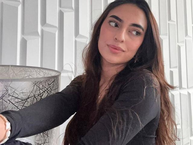 CelesteLarson ha lunghi capelli castani, un viso carino, e indossa una maglietta nera, guardando di lato con un leggero sorriso. Il suo seno è parzialmente visibile..