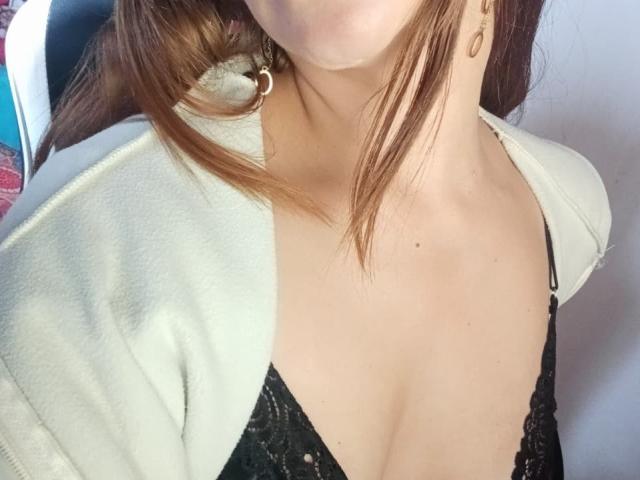 Crisht's chest, showing a black lace bra, with her white jacket open, exposing her tits. She has brown hair, a silver earring, and a light skin tone.