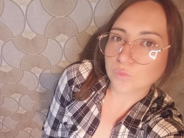 TinaEves with puffy lips, wearing glasses and a black-and-white plaid shirt, has a cute, chubby face and brown hair, looking directly at the camera.