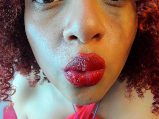 VioletaSwitch's face, focused on her red, glossy lips with visible lip texture. She has curly, red hair and a light brown skin tone. Her nose is slightly upturned.