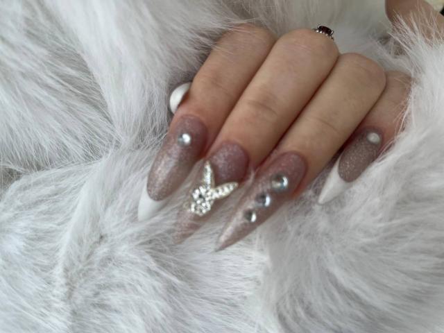 FallenAngelia's hands with long, glittery, pink-nude nails, white tips, and silver rhinestones, resting on white, fluffy fur. She wears a small, silver ring on her index finger.