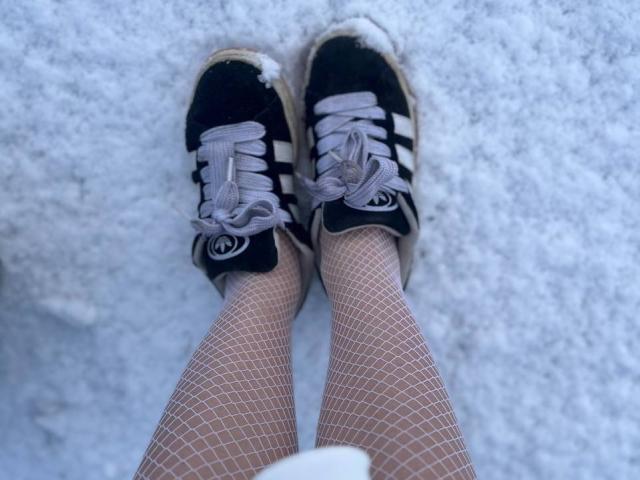 FallenAngelia's legs in white fishnet stockings, wearing black and white Adidas sneakers with gray laces, standing on a snowy ground, showing a small snowflake on each shoe.