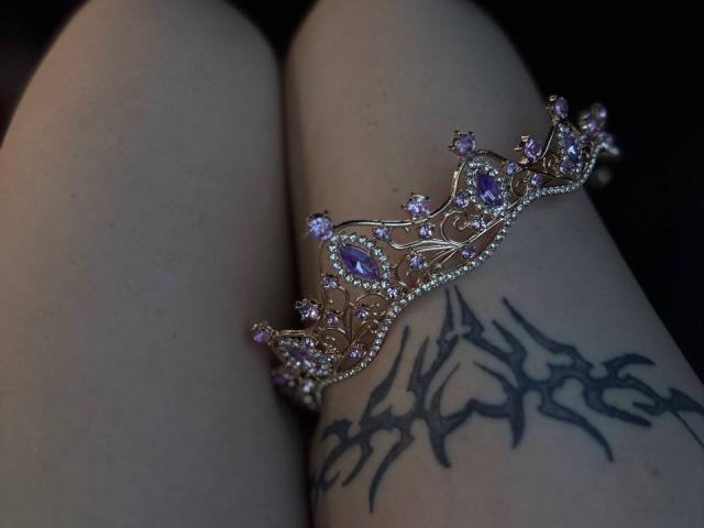 FallenAngelia's pale thighs with a purple and gold jeweled crown bracelet on her right thigh, showcasing a black tribal tattoo. Her smooth skin contrasts with the detailed jewelry.