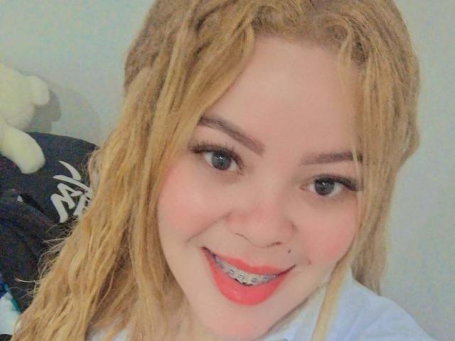 Sharicke69 has blonde dreads, blue eyes, and a cute smile with metal braces. She's wearing a white shirt and has a small nose piercing. Her ass is not visible.