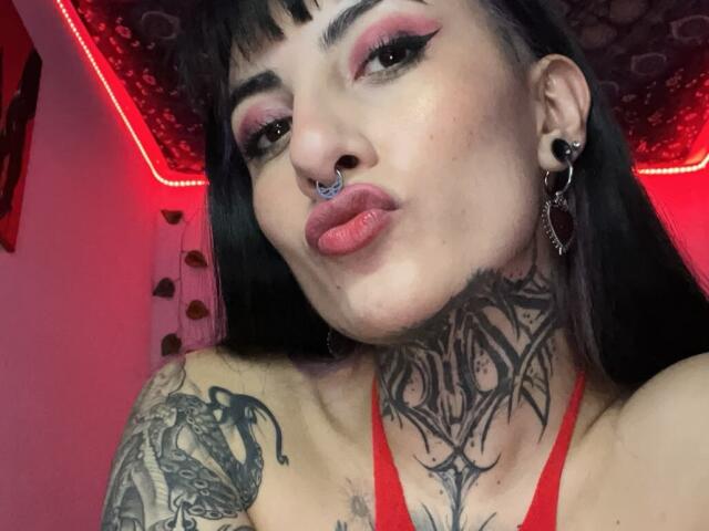LiaMiss heeft zwart haar, roze eyeliner en een neusring, met tatoeages op haar nek en arm. Ze frumelt met haar roze lippen, draagt rode oorbellen en een rode top..