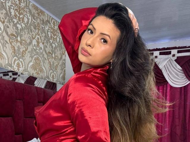 HannaRobertss with long brown hair, red satin shirt, looking over shoulder, hand in hair, sexy brown eyes, soft makeup, red and white room, red curtains, white ceiling.