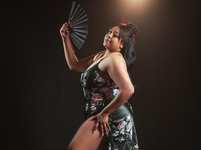 BiancaForest, con pechos de tamaño medio, vestida con un vestido floral negro, sosteniendo un abanico, con el trasero ligeramente levantado, cabello oscuro, horquillas rojas, ojos cerrados, luciendo sexy, fondo oscuro..