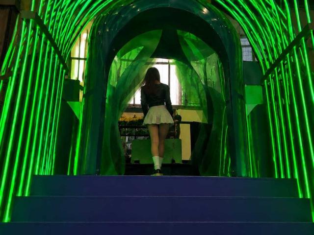 MiluSantoro's ass in a short, frilly white skirt, standing on blue stairs, back to camera, green neon arches, wearing a black top and white socks, in a dark room.