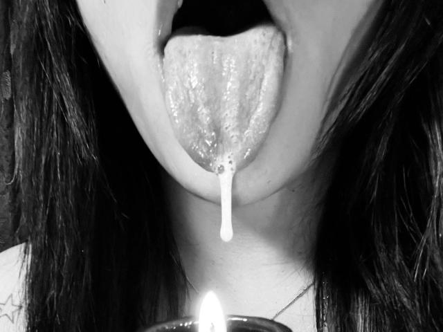 SophieBanksX's tongue is out with a drip of saliva hanging down, a small lit candle is in the bottom foreground. Black and white photo.