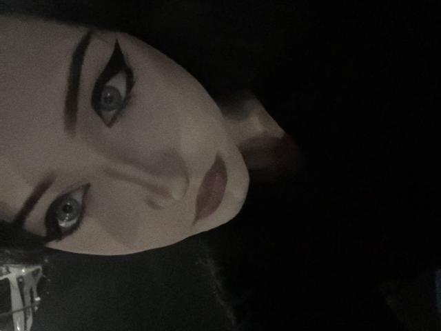 El rostro de KiraLowkey, con ojos oscuros, delineador negro grueso, piel pálida y labios rosados, cabello negro y un fondo sombrío. Sus senos no son visibles en esta toma..