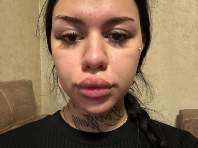 NatividadSpane has a shiny face with dark eyebrows, long eyelashes, small nose, and pink lips. She has black hair in a ponytail, a black ribbed shirt, and a tattoo.