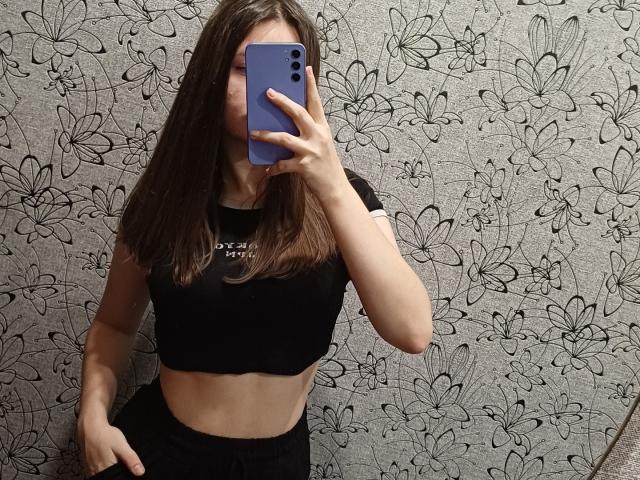 CathrynJacquet with brown hair, black crop top, and black pants, holding a blue phone, covering her face, showing her toned midriff and small tits.