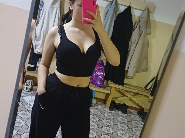 CathrynJacquet with big tits in a black sports bra and black Nike sweatpants, taking a mirror selfie with a pink phone in a locker room.