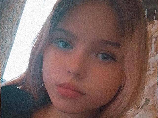 MaximaLasley has light brown hair, blue eyes, and pink lips with a slightly pouty expression. Her face is centered, and she's wearing a black top.