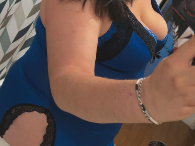El vestido azul de LadyDark69 con encaje negro, que muestra sus senos, un brazo con una pulsera de plata, cabello negro y una sección de encaje recortada en el lateral del vestido..