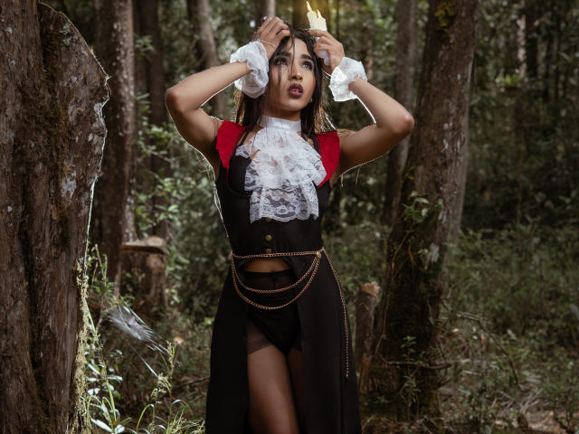 GabySantos with dark hair, red sleeves, black dress, white lace collar, hands in hair, forest background, black panties, gold chain, medium tits, sexy, standing, forest floor.