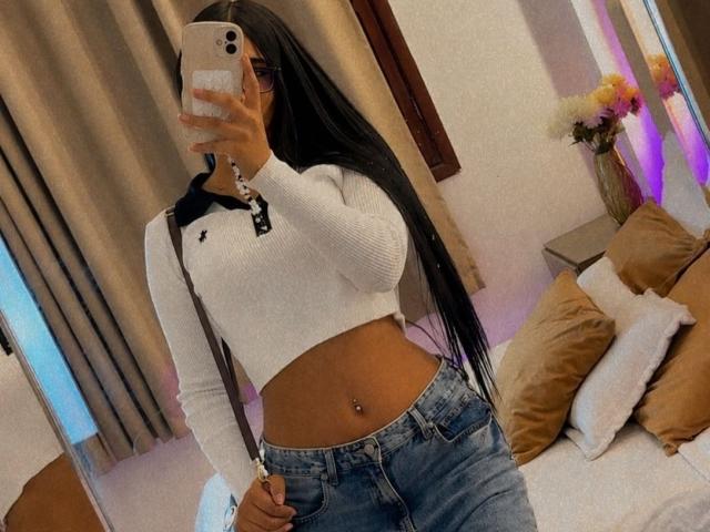 AntonellaMonroe with long black hair, white Under Armour crop top, blue jeans, navel piercing, holding phone in front of mirror, covering face. Boobs, butt not visible.